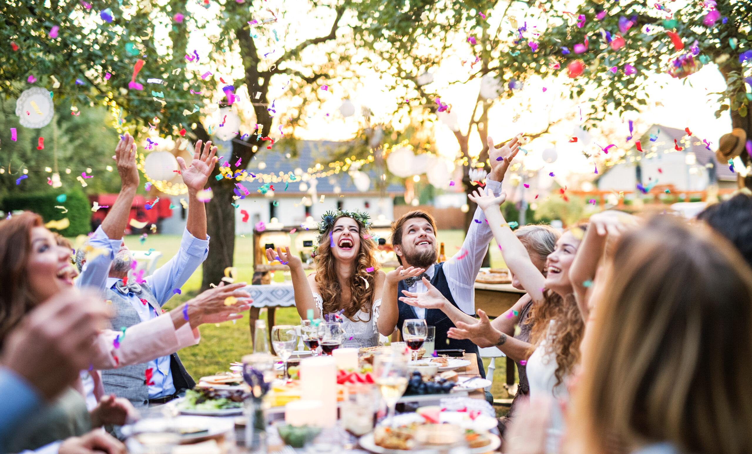 Wedding reception outside in the backyard. Bride and groom with family and guests sitting around the table, having fun.